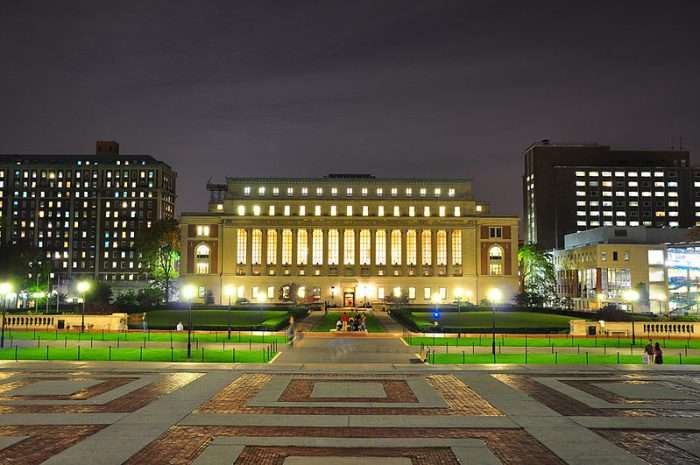 The library at Columbia University is lit up at night at the end of a path.