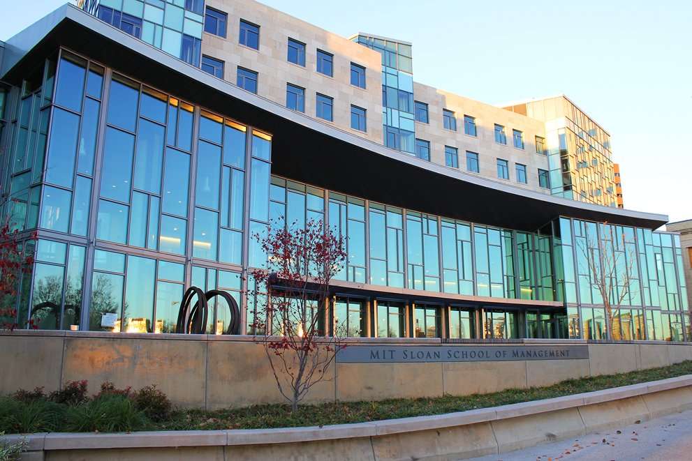 The glass facade of MIT's Sloan School building is featured.