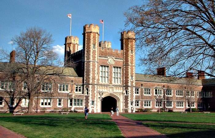 A lawn is featured in front of a brick building with two flags flying overhead at Washington University in St. Louis.